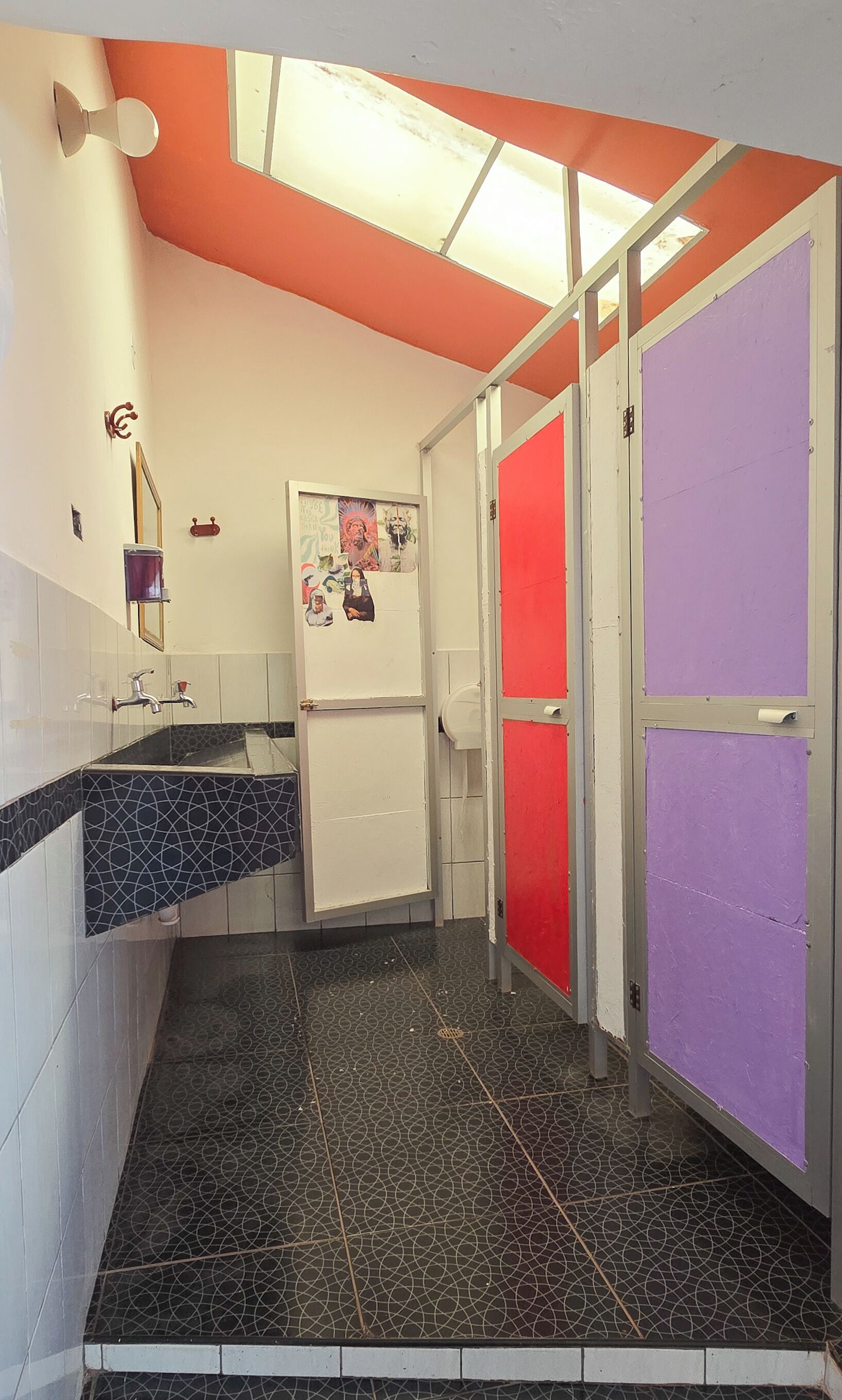 Un baño con piso de baldosas blanco y negro, un lavamanos con espejo y un refrigerador con un cartel.