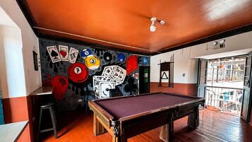 Una mesa de billar en una habitación con piso de madera y una pared decorada con diversas cartas de juego y dados.