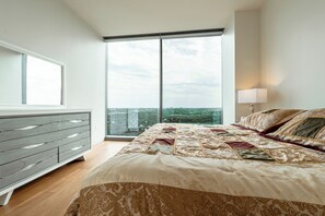Relax in a spacious bedroom with a large bed and city view, featuring a quilted headboard and minimalist dresser.