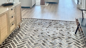 A spacious living area with a large window overlooking a body of water, a modern fireplace, and a herringbone-patterned rug. - Fully remodeled lake house with gorgeous views of Bull Shoals Lake! (Lakeview)