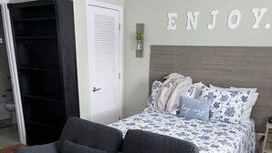 A bedroom with a bed, a grey sofa, a wardrobe, and a wall with the word "ENJOY". - Cozy Condo Steps from the Gulf. Private, quiet but minutes from everything. (Biloxi)