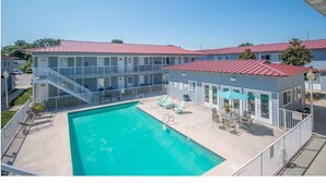 A hotel with a swimming pool, outdoor seating, and a red-roofed building. - Cozy Condo Steps from the Gulf. Private, quiet but minutes from everything. (Biloxi)