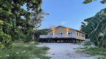 Une maison à deux étages dotée d’un balcon, entourée d’une végétation tropicale.