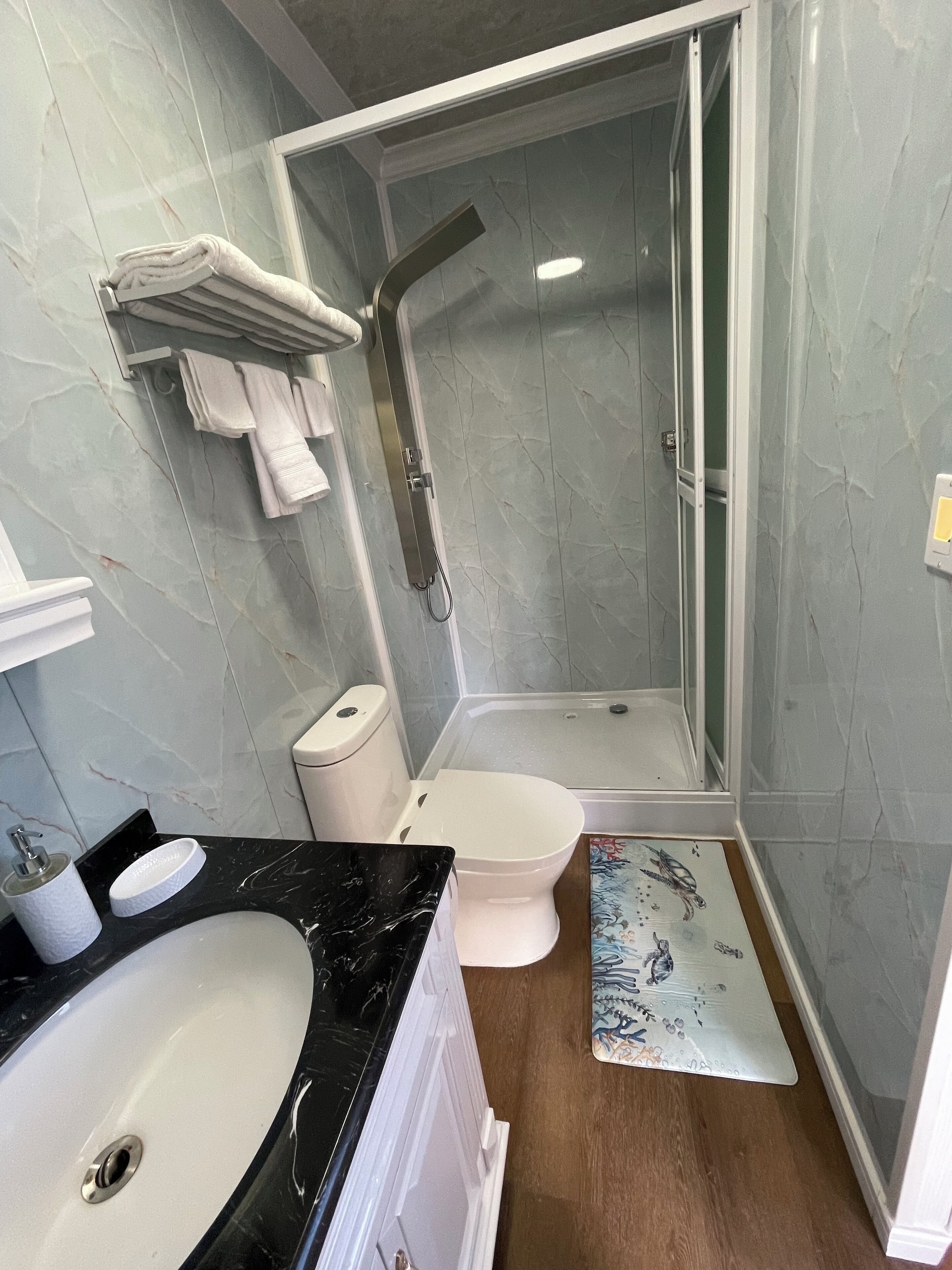 Un baño con lavamanos de mármol, inodoro y ducha con mampara de vidrio.
