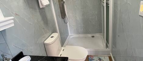 Un baño con lavamanos de mármol, inodoro y ducha con mampara de vidrio.
