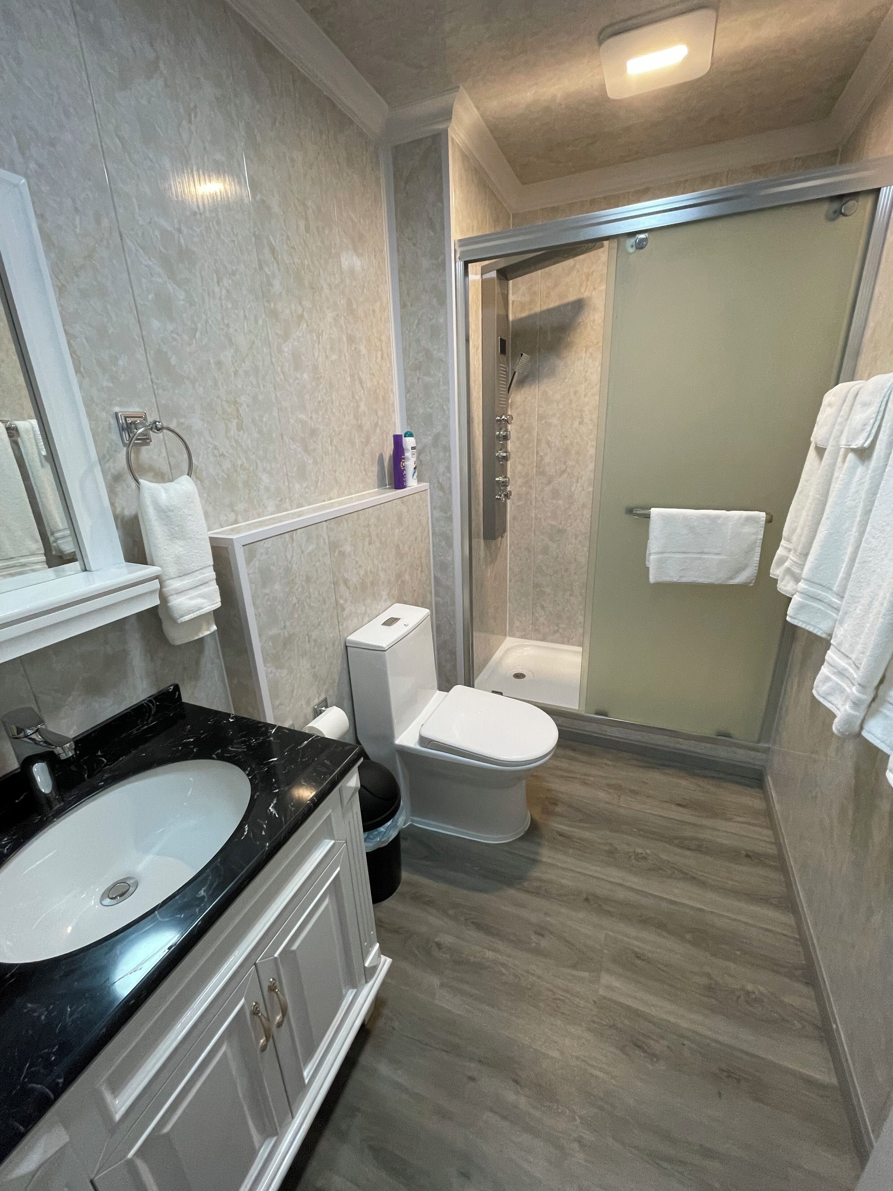 Une salle de bain moderne avec un lavabo en marbre noir, des toilettes blanches et une douche séparée par des parois en verre.