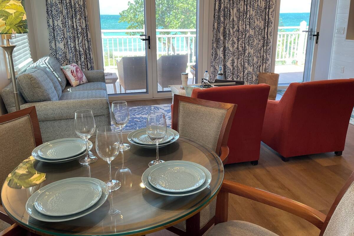Un coin repas avec une table en verre, dressée pour quatre personnes, entourée de chaises rouges et beiges.