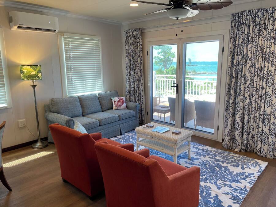 A living room with a grey sofa, red armchairs, a coffee table, and a view of the ocean through large sliding doors.