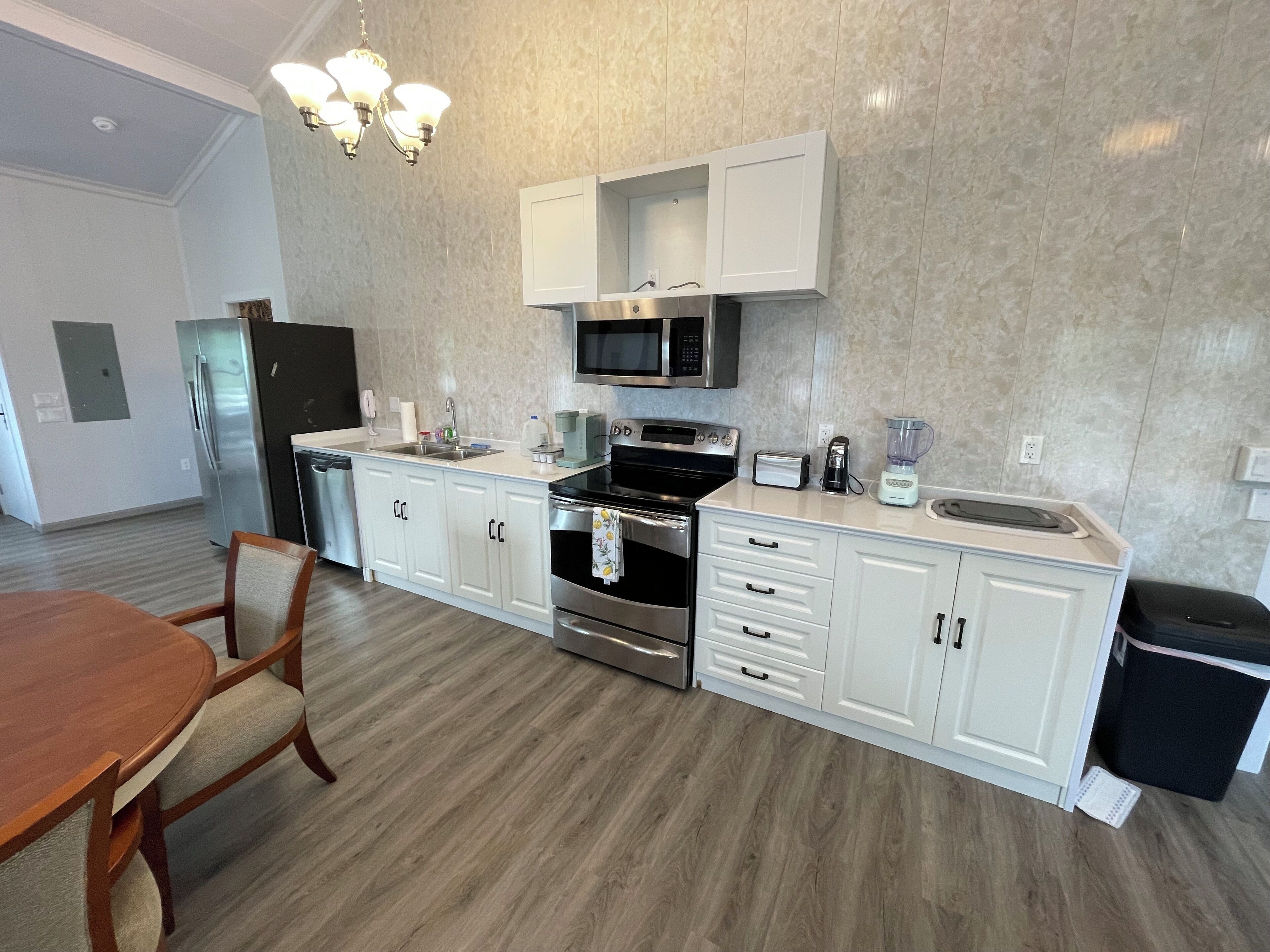 A modern kitchen with white cabinets, stainless steel appliances, and a wooden dining table.