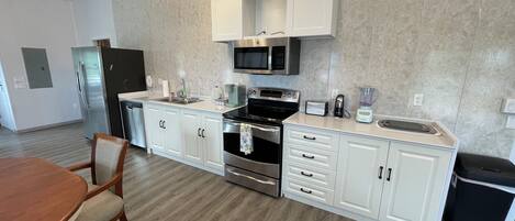 A modern kitchen with white cabinets, stainless steel appliances, and a wooden dining table.