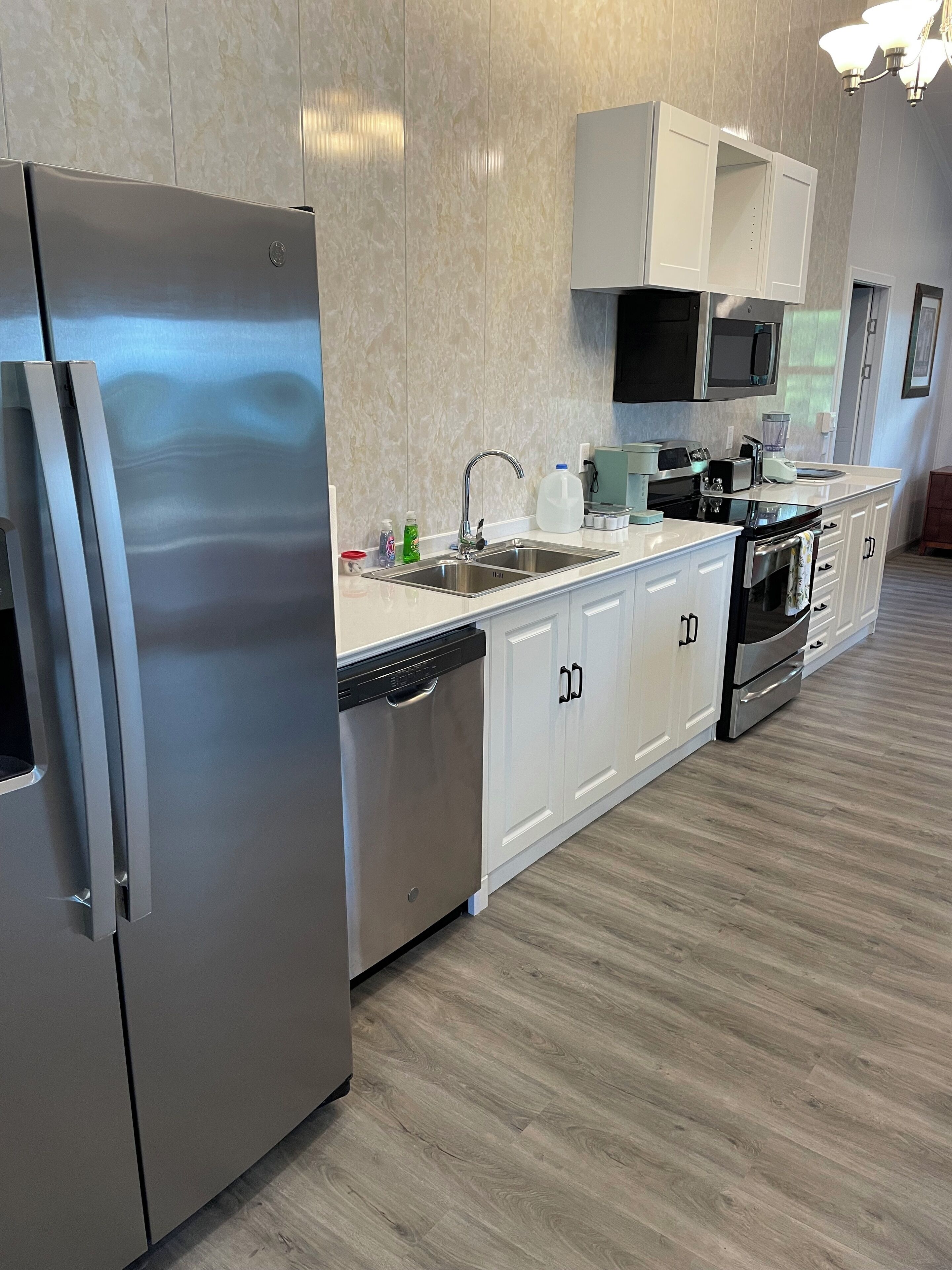 Una cocina moderna con electrodomésticos de acero inoxidable, armarios blancos y piso de madera.