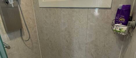 A shower area with a window, a hand dryer, and toiletries on a shelf.