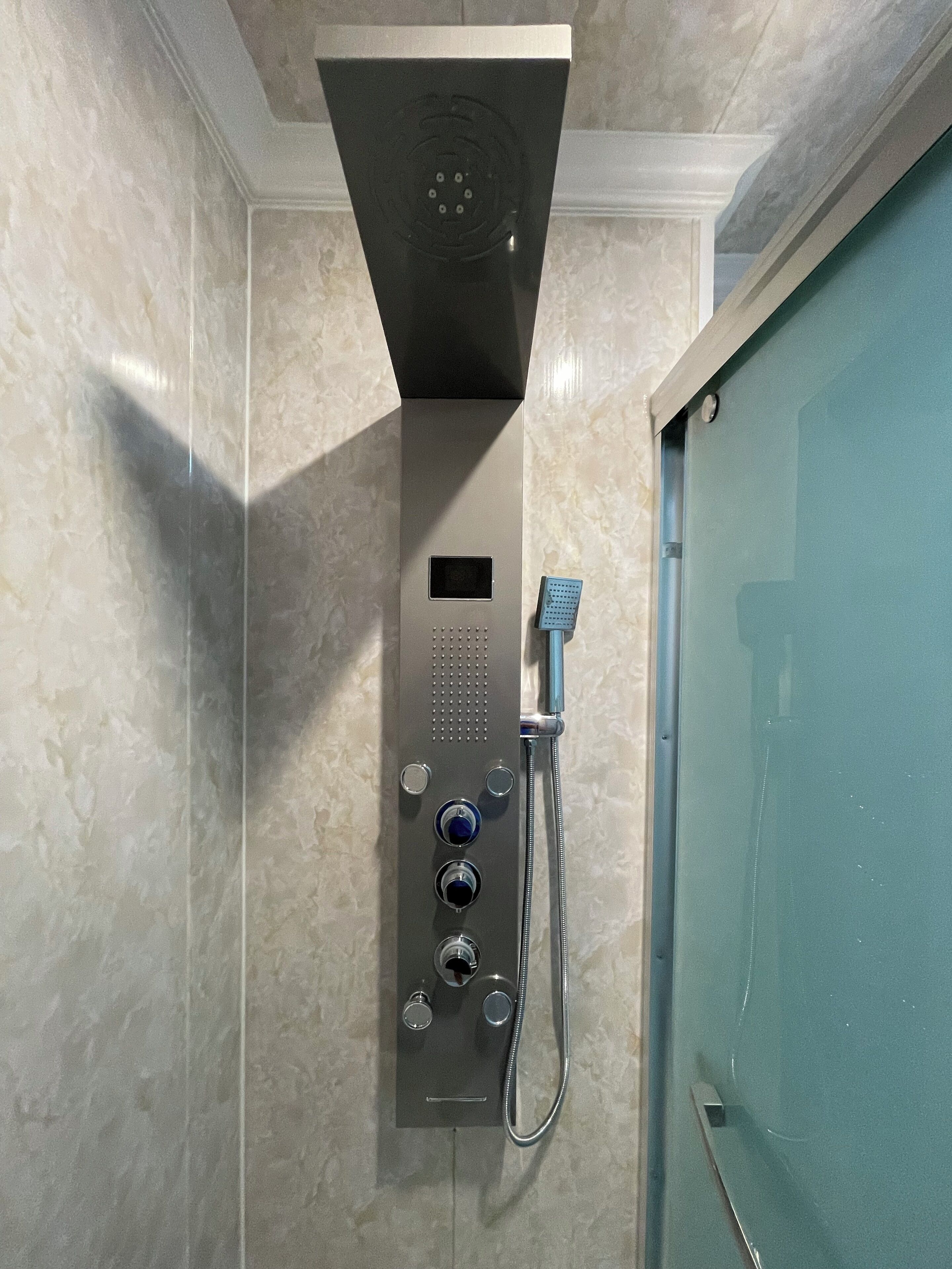 A modern shower with a control panel, a handheld showerhead, and a wall-mounted faucet.