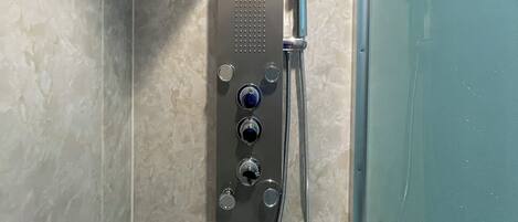 A modern shower with a control panel, a handheld showerhead, and a wall-mounted faucet.
