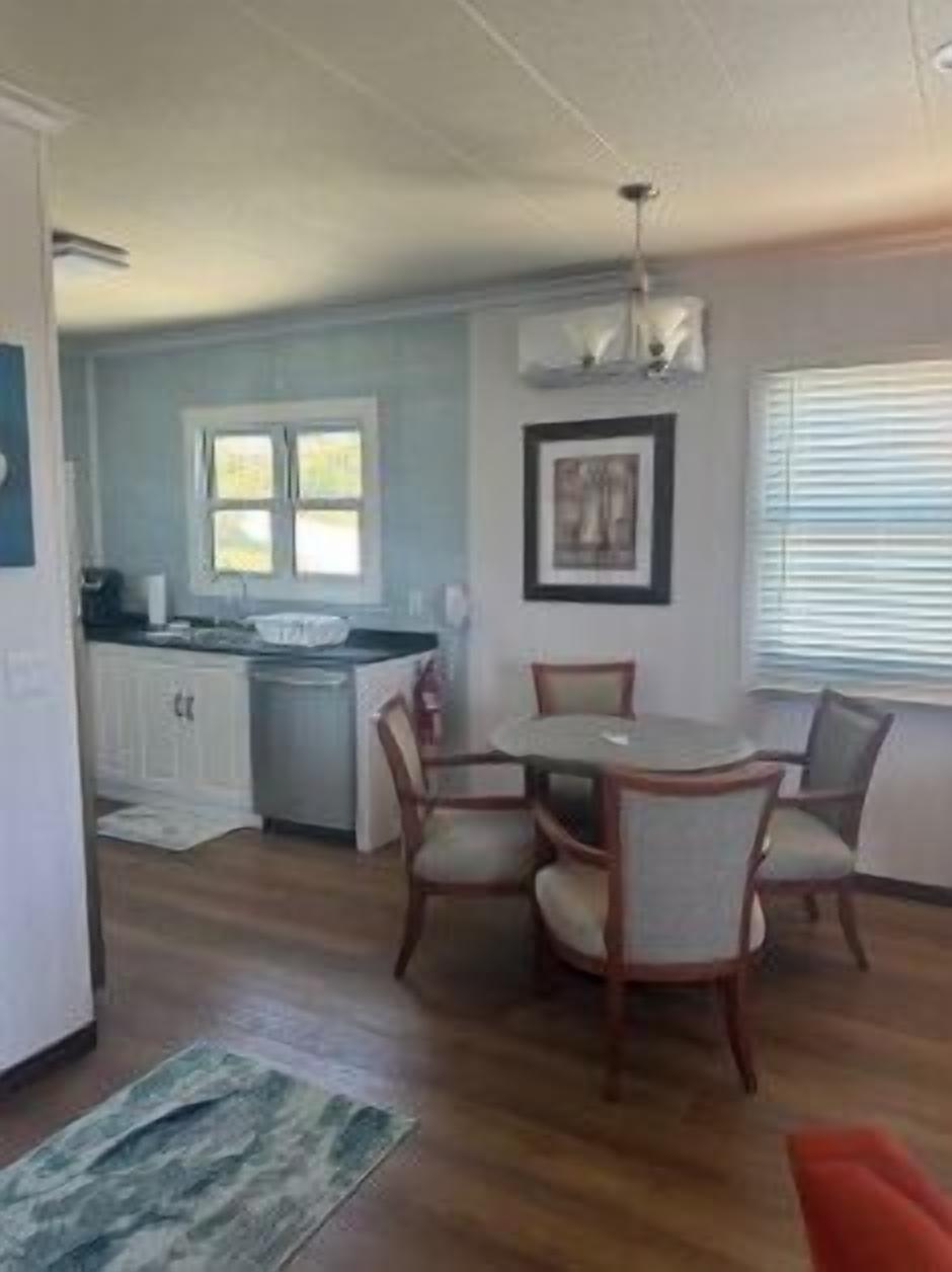 A dining area with a round table and chairs, a kitchen with white cabinets, and a window with blinds.