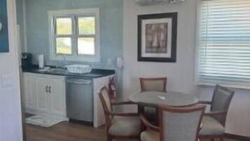 A dining area with a round table and chairs, a kitchen with white cabinets, and a window with blinds.