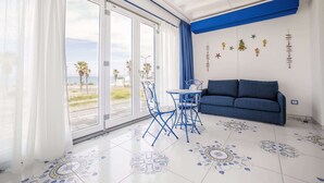 Une pièce avec un canapé bleu, une table entourée de chaises et une vue sur des palmiers, visible à travers de grandes fenêtres.