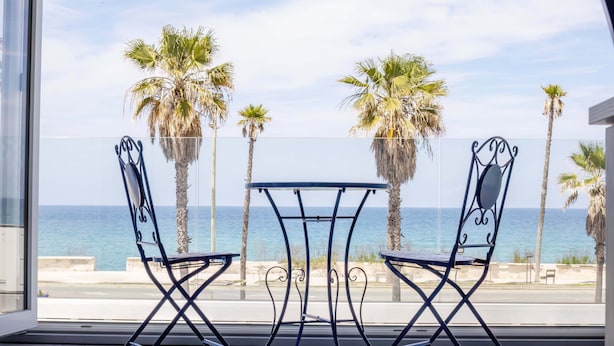 Un balcon avec deux chaises et une table, d’où l’on peut admirer la mer et les palmiers.