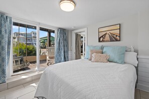 A bedroom with a large bed, a view of the outside, and a painting on the wall. - Ocean View, Private Heated Pool, 6BR, 4BA, Sleeps 14. Fall Getaway Package. (Holden Beach)