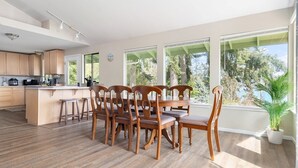 Moderni keittiö, jossa on puiset kaapit, keskellä sijaitseva keittiösaareke sekä ruokailutila, jossa on puiset tuolit ja pöytä.