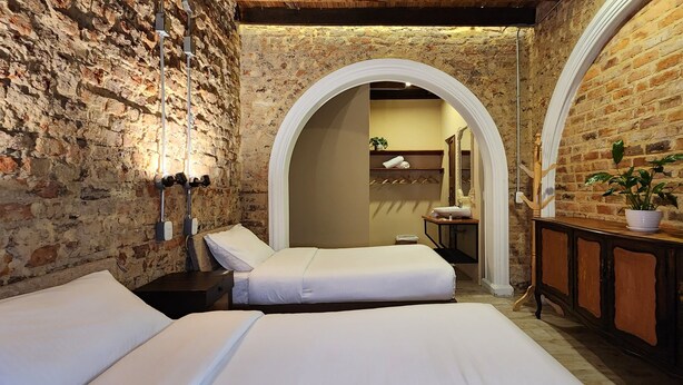 Quarto com duas camas, um armário de madeira e uma parede de tijolos.