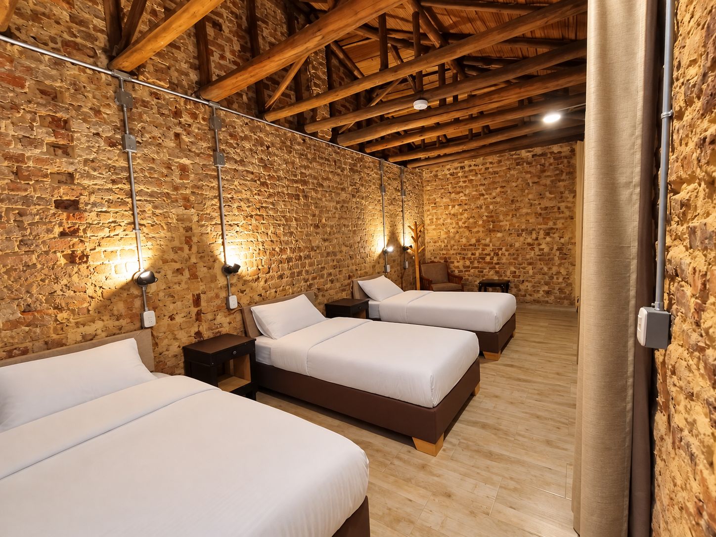 A room with three beds, wooden beams, stone walls, and wall-mounted lighting.