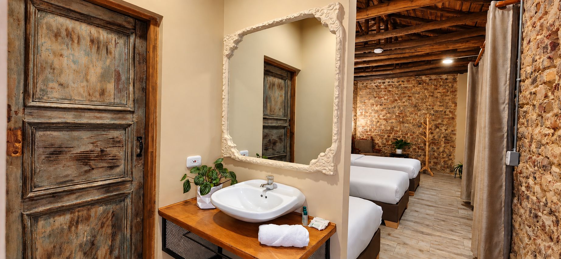 A bathroom with a wooden vanity, a large mirror, and a white sink. There are two beds visible in the background.