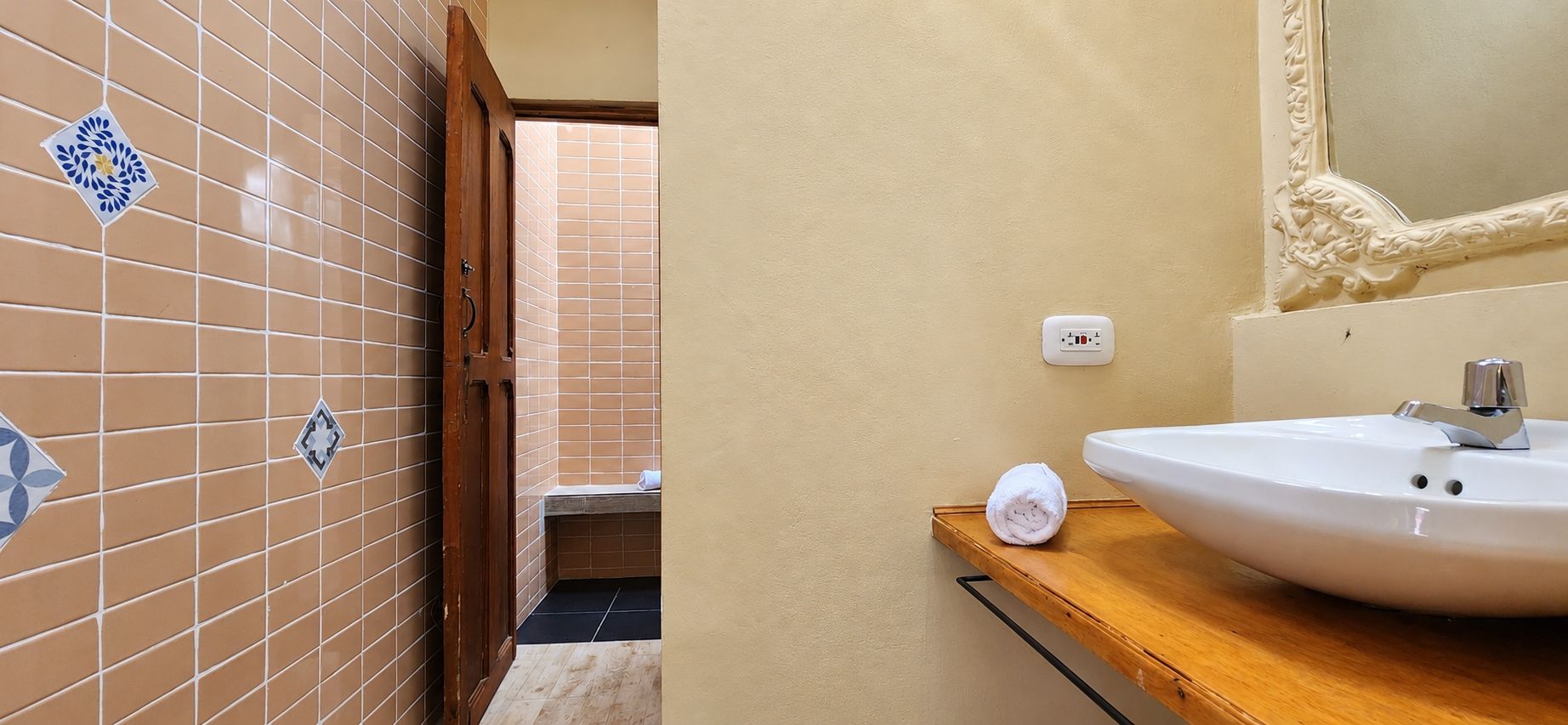 A bathroom with a white sink, a mirror with an ornate frame, and a door leading to a shower area.