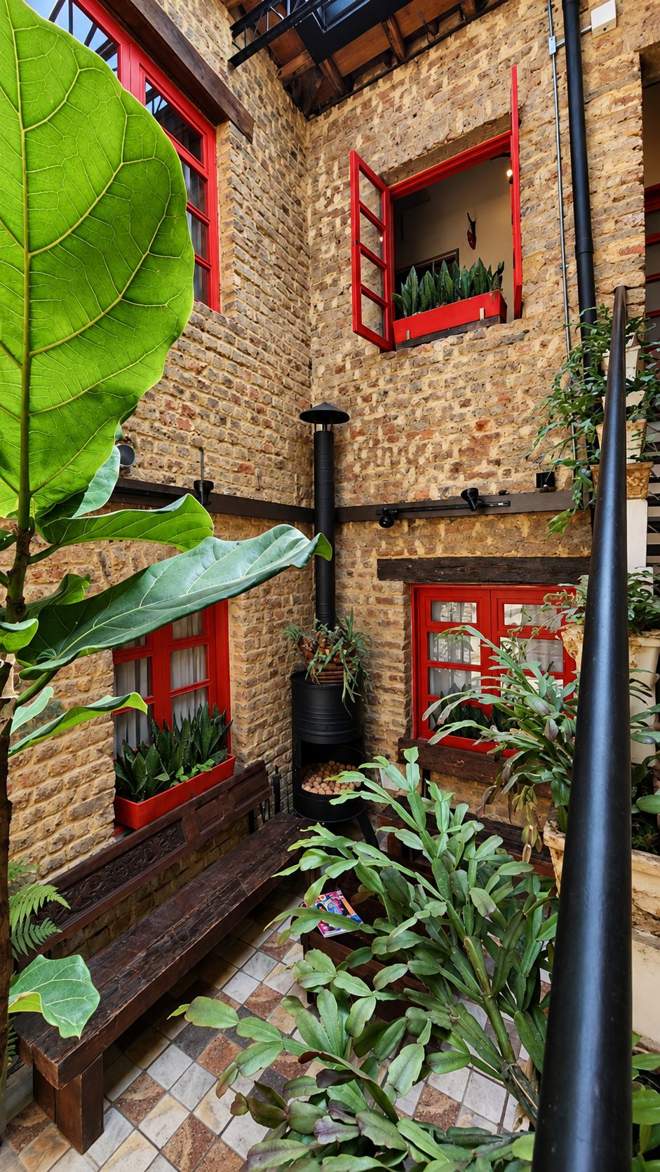 Un patio con muro de piedra, ventanas de marco rojo y plantas en macetas.