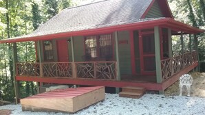 Eine Hütte mit roter und grüner Fassade, einer Veranda mit Geländer und einem kleinen Holzboden.