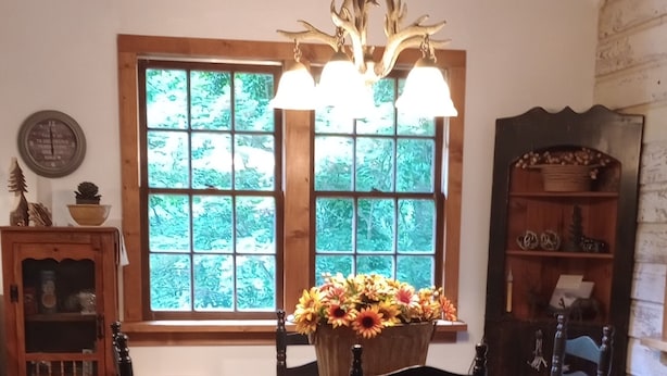 Ein Essbereich mit einem Holztisch, vier Stühlen, einer Chandelierleuchtre und einem Fenster mit Blick auf Bäume.