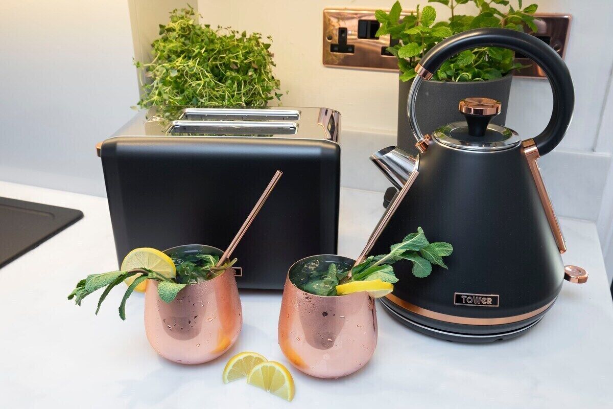 Une cuisine avec un grille-pain noir, une bouilloire noire et deux mugs en cuivre, garnis de feuilles de menthe et de rondelles de citron.