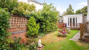 A garden with a brick wall, a wooden fence, and a small shed. - Luxurious 1 Bed Detached Home with Gated Parking (Cheltenham)