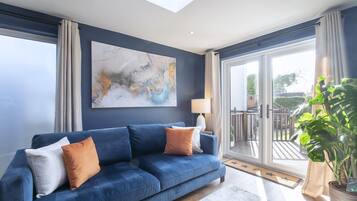 A modern living room with a blue sofa, a large abstract painting, and a view of the outdoors through a sliding glass door.