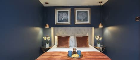 A neatly arranged bedroom with a large bed, two framed pictures on the wall, and a tray with a teapot and cups on the bed.