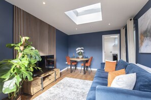 Una sala de estar moderna con un sofá azul, una mesa de comedor con sillas, una planta grande y un tragaluz.