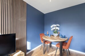 Een eetruimte met een ronde houten tafel, twee oranje stoelen en een blauwe wand.