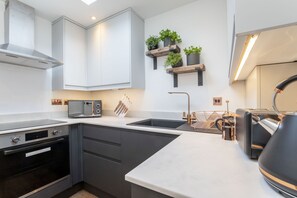 Una cocina moderna con horno empotrado, microondas y pileta. Hay estantes de madera con plantas, una cafetera y un hervidor sobre la encimera.