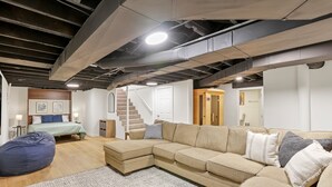 Una sala de estar moderna con un sofá modular, un sillón de peluche y una escalera que lleva a un nivel superior.