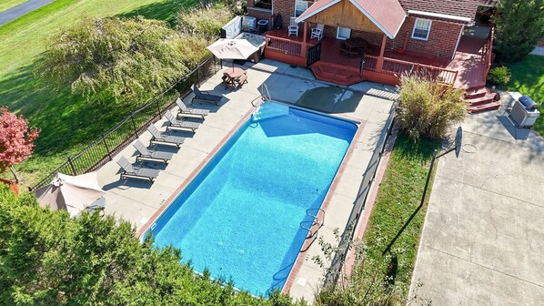 Una piscina rettangolare con solarium, circondata da una recinzione e una casa con portico.
