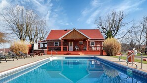 Una piscina con sillones de descanso y un edificio con techo rojo al fondo.