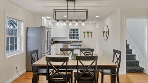Una cocina moderna con una isla central, armarios blancos y un comedor con sillas de madera.