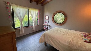 Un dormitorio con cama, una ventana con cortinas, un espejo redondo y techo de madera.