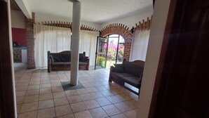 Una sala de estar con suelo de baldosas, un sofá, una silla y un ventanal de vidrio que da a un balcón.