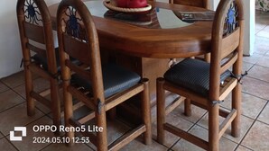 Un comedor con una mesa redonda de madera, cuatro sillas con elaborados diseños en el respaldo, un cuadro abstracto rojo, un techo de azulejos y un arco de ladrillo que conduce a otra habitación.