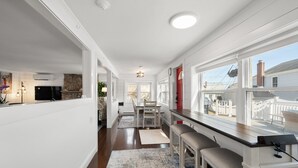 A spacious kitchen with a long counter, a dining area with a table and chairs, and large windows offering a view of the outside. - Beach Cottage, private beach and pass (East Lyme)