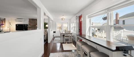 A spacious kitchen with a long counter, a dining area with a table and chairs, and large windows offering a view of the outside.