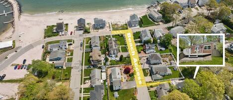 Vue aérienne d’une zone résidentielle côtière, avec des maisons, une plage et un sentier balisé indiquant l’accès à la plage.
