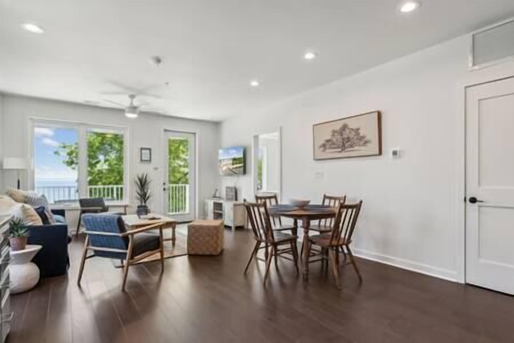 A spacious living room with a dining area, large windows, and a ceiling fan.