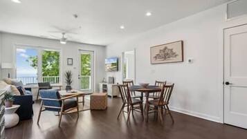 A spacious living room with a dining area, large windows, and a ceiling fan.